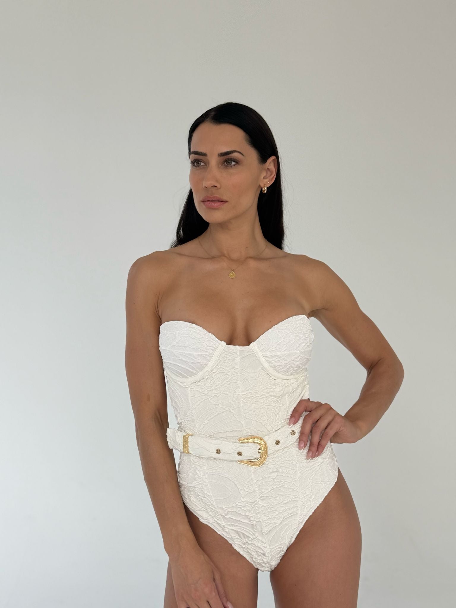 model wearing high quality designer luxury white one-piece swimsuit with accented belt for a snapped smaller waist look